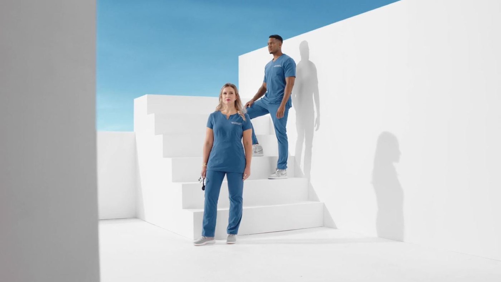 Two people in blue scrubs on white stairs